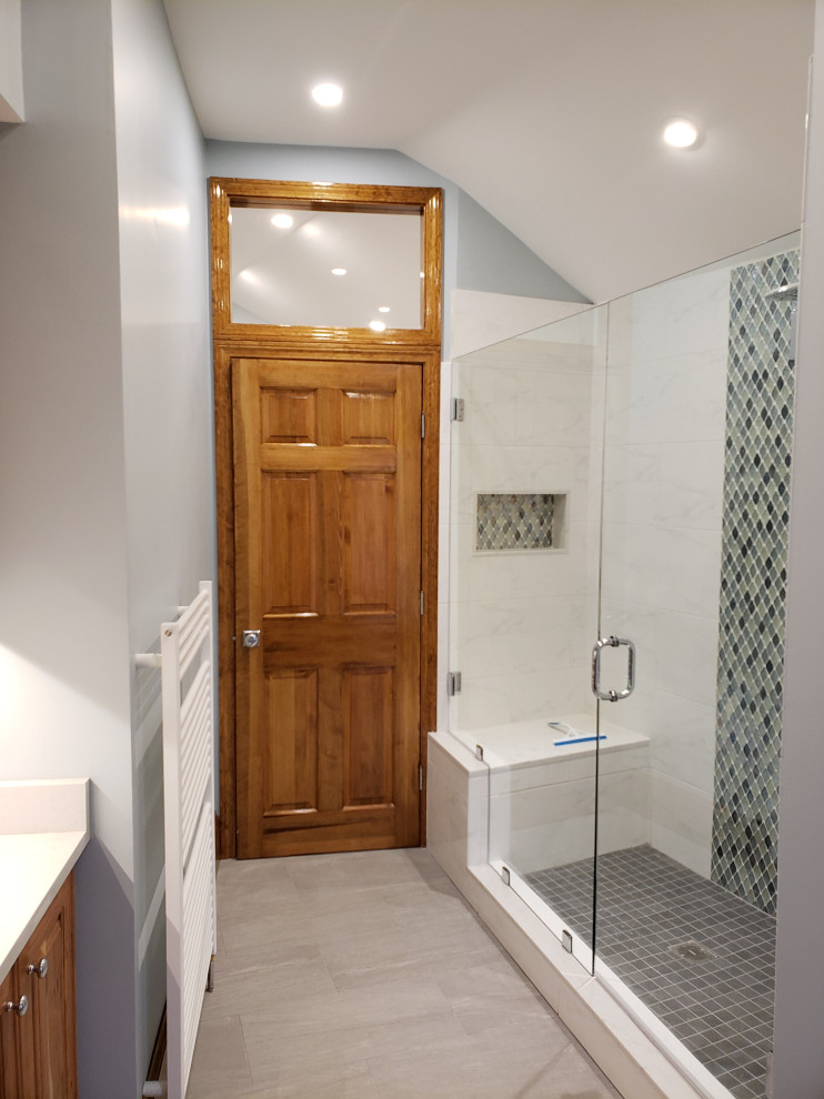 This is an example of a mid-sized contemporary master bathroom in Boston with raised-panel cabinets, medium wood cabinets, an alcove shower, a bidet, white tile, marble, blue walls, ceramic floors, an undermount sink, engineered quartz benchtops, grey floor, a hinged shower door, white benchtops, a laundry, a double vanity, a built-in vanity and vaulted.