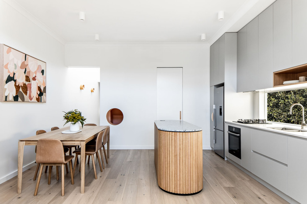 Contemporary galley eat-in kitchen in Sydney with a double-bowl sink, flat-panel cabinets, grey cabinets, quartz benchtops, window splashback, stainless steel appliances, medium hardwood floors, with island, brown floor and white benchtop.
