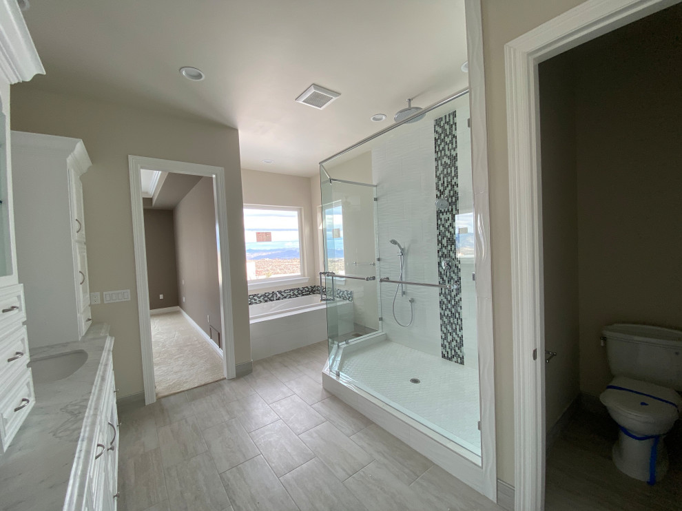 Inspiration for an expansive modern master bathroom in Other with raised-panel cabinets, white cabinets, an undermount tub, an alcove shower, a one-piece toilet, black and white tile, glass tile, beige walls, porcelain floors, an undermount sink, marble benchtops, grey floor, a hinged shower door and white benchtops.