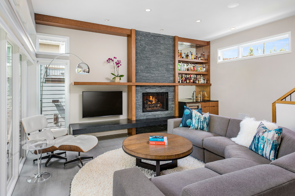 Large contemporary living room in Chicago with a home bar, beige walls, a wall-mounted tv, a standard fireplace, porcelain floors and a stone fireplace surround.