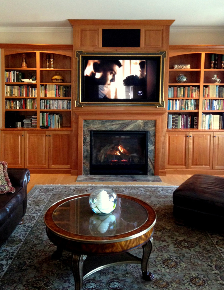 Inspiration for a traditional family room in Boston with a library, light hardwood floors, a standard fireplace, a wood fireplace surround and a concealed tv.
