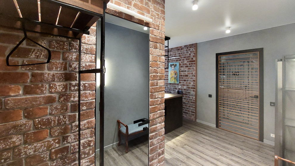 Exemple d'une grande entrée industrielle avec un couloir, un mur gris, un sol en bois brun, une porte simple, une porte grise, un sol marron et un mur en parement de brique.