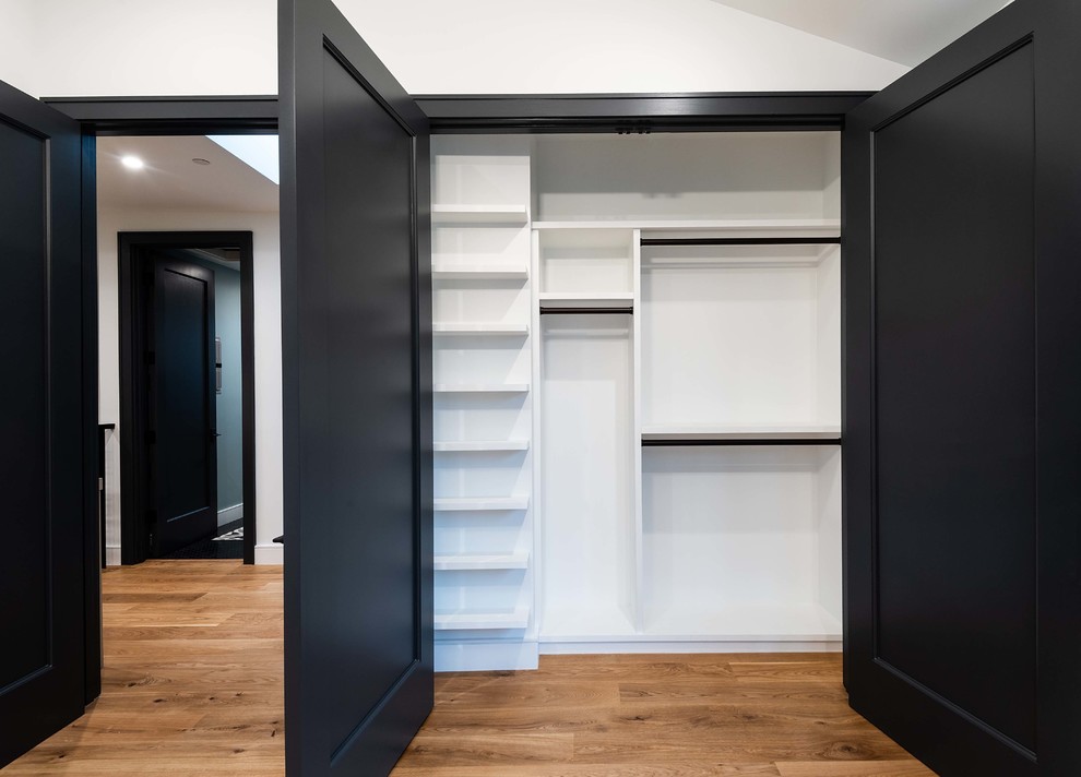 This is an example of a mid-sized modern gender-neutral built-in wardrobe in Los Angeles with white cabinets, medium hardwood floors and brown floor.