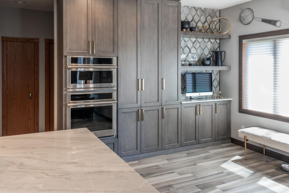 Large transitional medium tone wood floor and brown floor kitchen photo with a single-bowl sink, flat-panel cabinets, gray cabinets, quartzite countertops, gray backsplash, marble backsplash, paneled appliances, an island and white countertops
