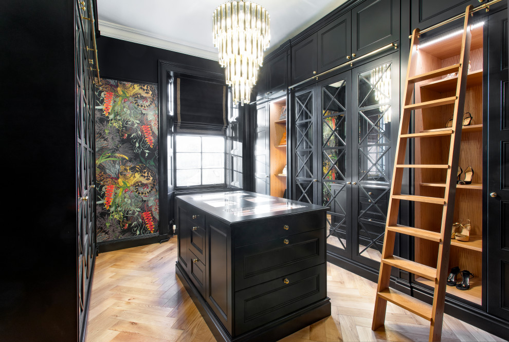 Design ideas for a large classic gender neutral dressing room in Edinburgh with glass-front cabinets, black cabinets, light hardwood flooring and beige floors.