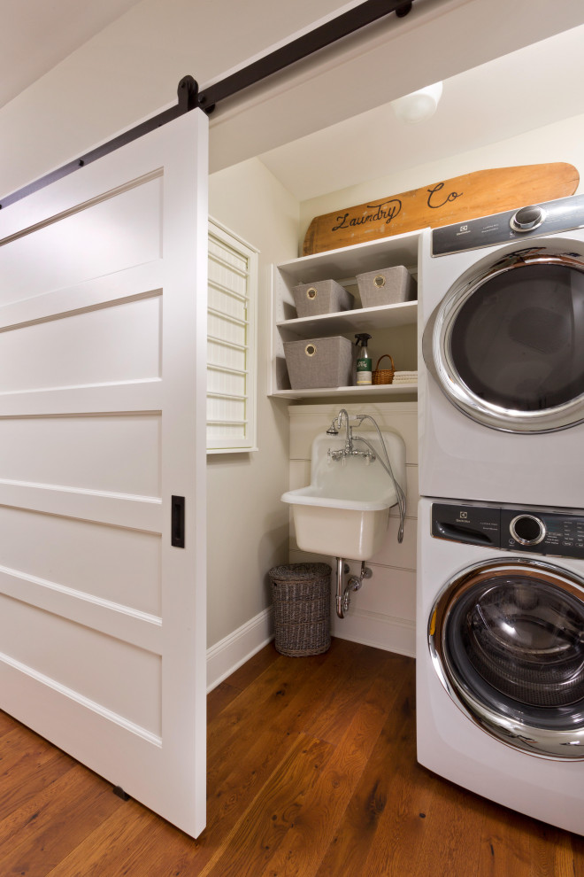 Large classic laundry cupboard in New York with a belfast sink, white splashback, tonge and groove splashback, grey walls, medium hardwood flooring, a stacked washer and dryer, brown floors and tongue and groove walls.