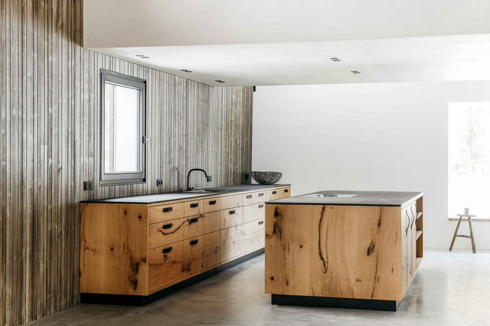 This is an example of an expansive country open plan kitchen in Munich with an undermount sink, flat-panel cabinets, medium wood cabinets, concrete floors, with island, grey floor, black benchtop and timber splashback.