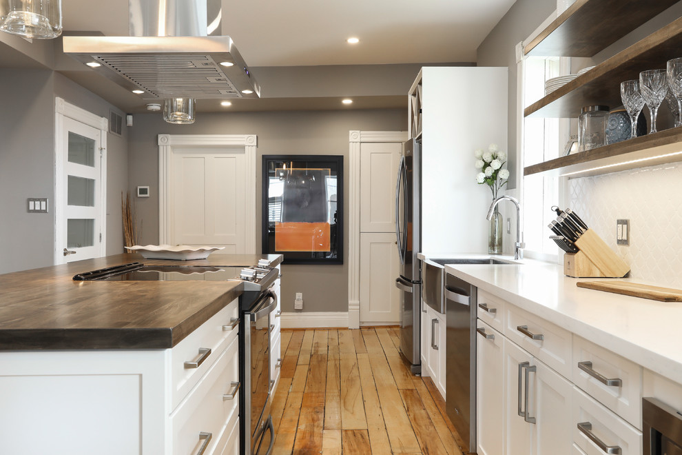 Inspiration for a mid-sized transitional single-wall medium tone wood floor and brown floor eat-in kitchen remodel with a farmhouse sink, shaker cabinets, white cabinets, white backsplash, stainless steel appliances, an island and white countertops