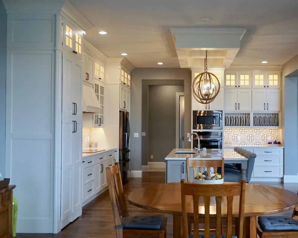 Kitchen pantry - large transitional l-shaped medium tone wood floor kitchen pantry idea in Cedar Rapids with an undermount sink, shaker cabinets, white cabinets, quartz countertops, multicolored backsplash, cement tile backsplash, stainless steel appliances and an island