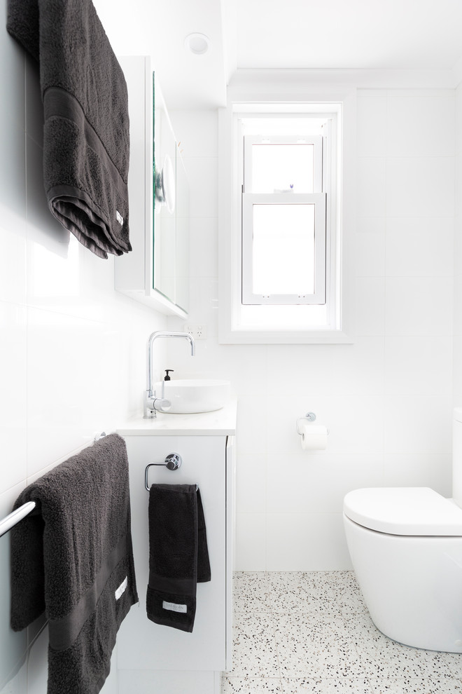Photo of a small contemporary 3/4 bathroom in Sydney with furniture-like cabinets, white cabinets, a drop-in tub, a corner shower, a wall-mount toilet, white tile, porcelain tile, white walls, porcelain floors, a vessel sink, engineered quartz benchtops, multi-coloured floor, an open shower and grey benchtops.