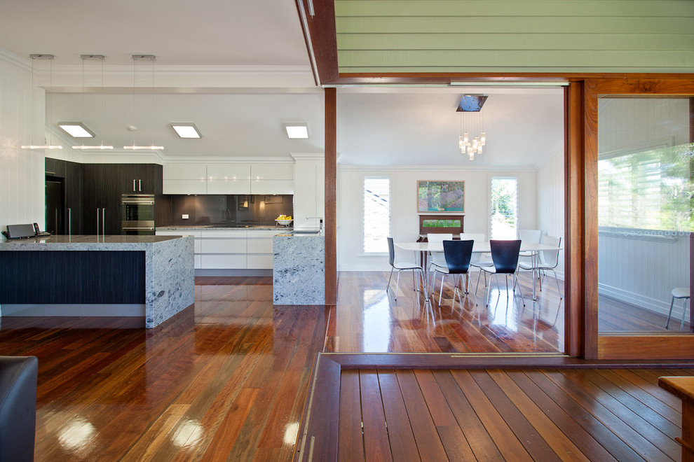 Inspiration for a small contemporary open plan kitchen in Brisbane with a double-bowl sink, flat-panel cabinets, white cabinets, limestone benchtops, black splashback, glass sheet splashback, stainless steel appliances, medium hardwood floors and a peninsula.