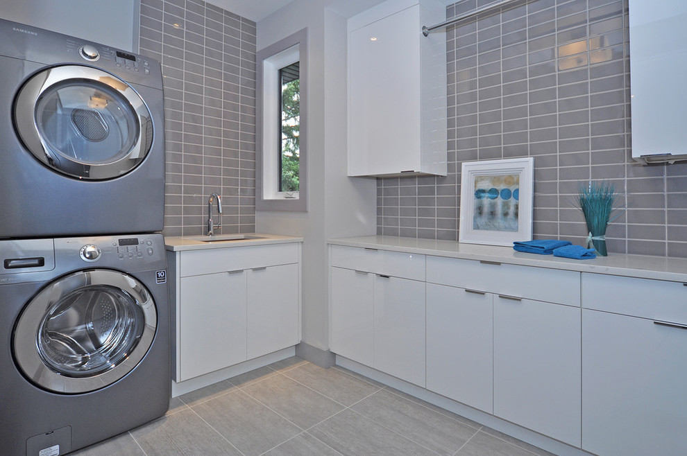 Design ideas for a mid-sized contemporary l-shaped dedicated laundry room in Calgary with an undermount sink, flat-panel cabinets, white cabinets, quartzite benchtops, grey walls, porcelain floors, a stacked washer and dryer and beige floor.