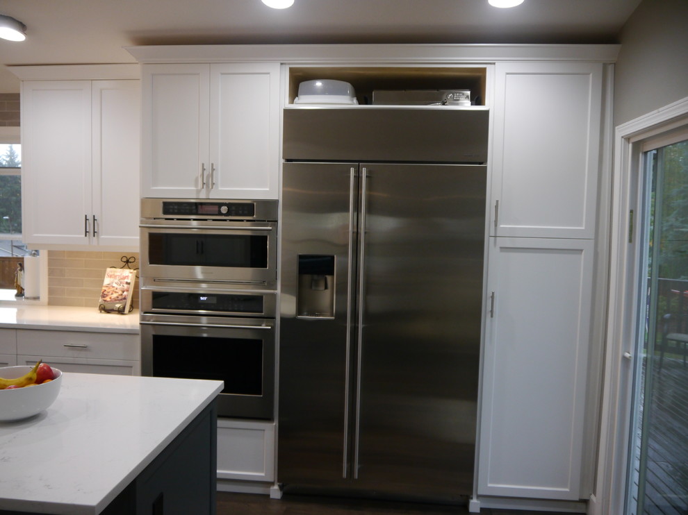 Eat-in kitchen - large transitional dark wood floor and brown floor eat-in kitchen idea in Seattle with a single-bowl sink, shaker cabinets, white cabinets, solid surface countertops, beige backsplash, ceramic backsplash, stainless steel appliances, an island and white countertops