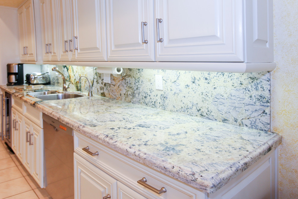 Photo of a large transitional galley eat-in kitchen in Miami with a double-bowl sink, raised-panel cabinets, white cabinets, granite benchtops, multi-coloured splashback, stone slab splashback, stainless steel appliances, with island and ceramic floors.