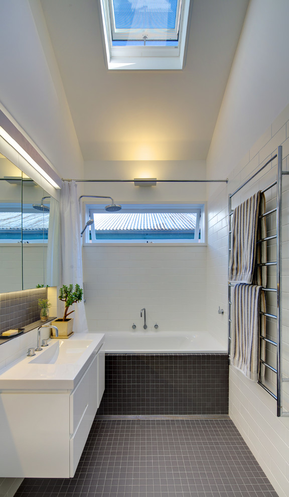 Design ideas for a mid-sized contemporary master bathroom in Sydney with an integrated sink, flat-panel cabinets, white cabinets, solid surface benchtops, an alcove tub, a shower/bathtub combo, gray tile, ceramic tile, white walls and mosaic tile floors.