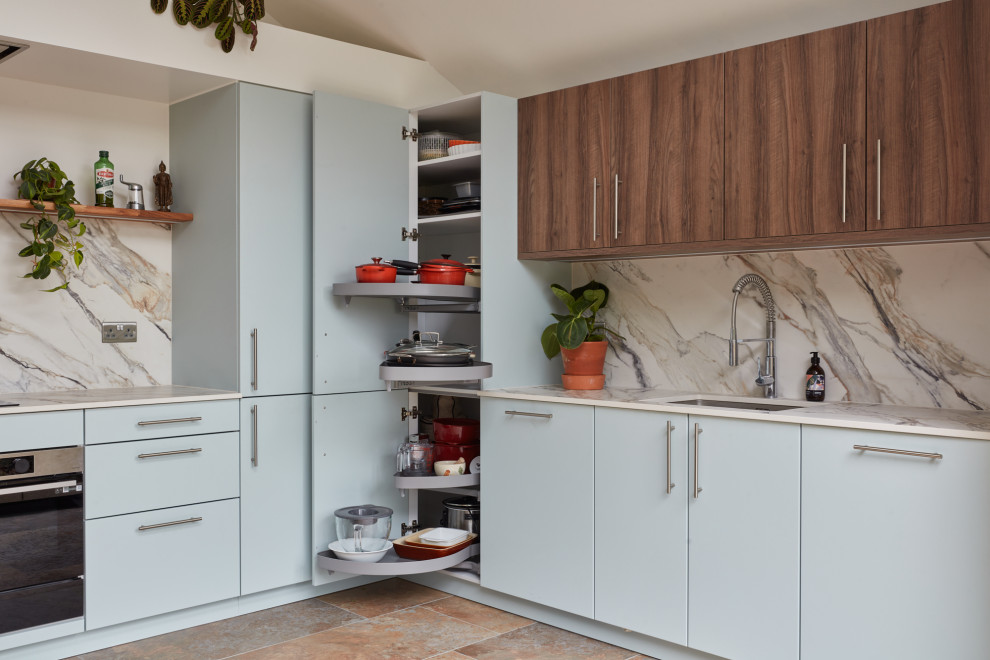 Inspiration for a mid-sized contemporary u-shaped eat-in kitchen in London with a drop-in sink, flat-panel cabinets, blue cabinets, solid surface benchtops, grey splashback, porcelain splashback, stainless steel appliances, slate floors, grey floor, grey benchtop and vaulted.