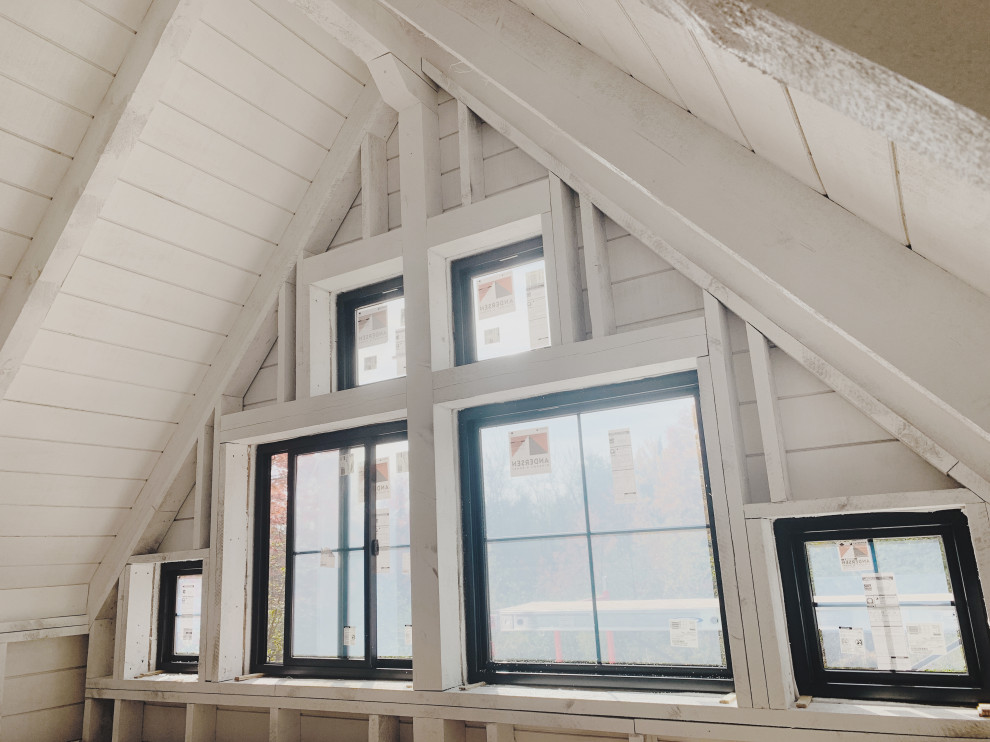 Kleines Uriges Schlafzimmer im Loft-Style mit weißer Wandfarbe, hellem Holzboden, Kaminofen, Kaminumrandung aus Holzdielen, beigem Boden, gewölbter Decke und Holzdielenwänden in Minneapolis