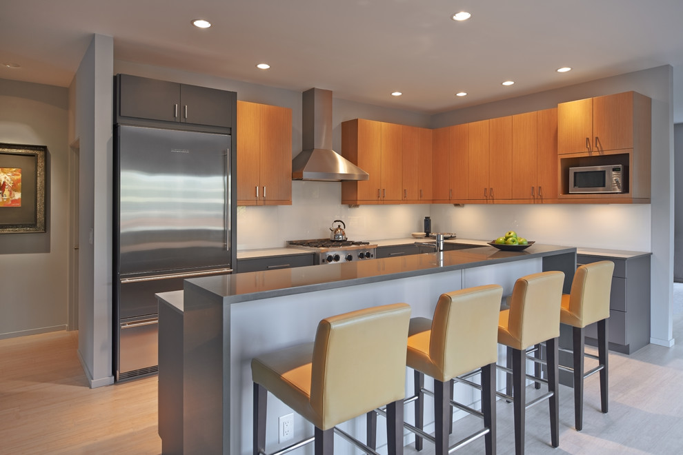Design ideas for a mid-sized contemporary l-shaped open plan kitchen in Seattle with with island, flat-panel cabinets, light wood cabinets, quartz benchtops, blue splashback, glass sheet splashback, stainless steel appliances, an undermount sink and bamboo floors.