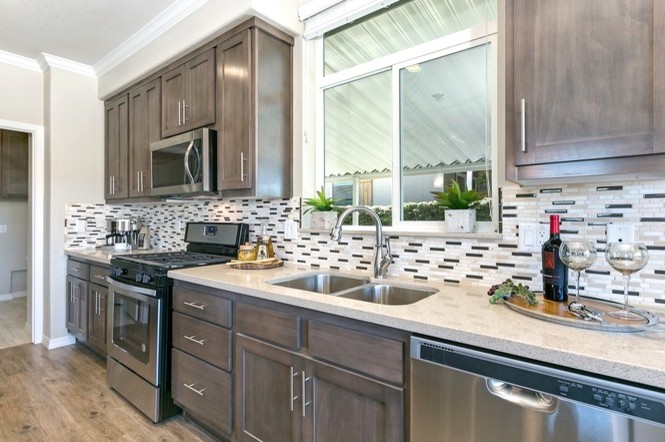 Mid-sized contemporary l-shaped open plan kitchen in San Diego with a double-bowl sink, raised-panel cabinets, brown cabinets, quartz benchtops, grey splashback, glass tile splashback, stainless steel appliances, medium hardwood floors, with island and brown floor.