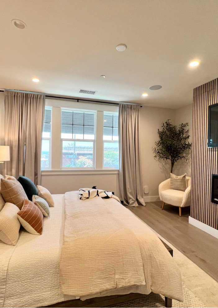 Design ideas for a mid-sized transitional master bedroom in Los Angeles with green walls, medium hardwood floors, a hanging fireplace, a wood fireplace surround, brown floor and panelled walls.