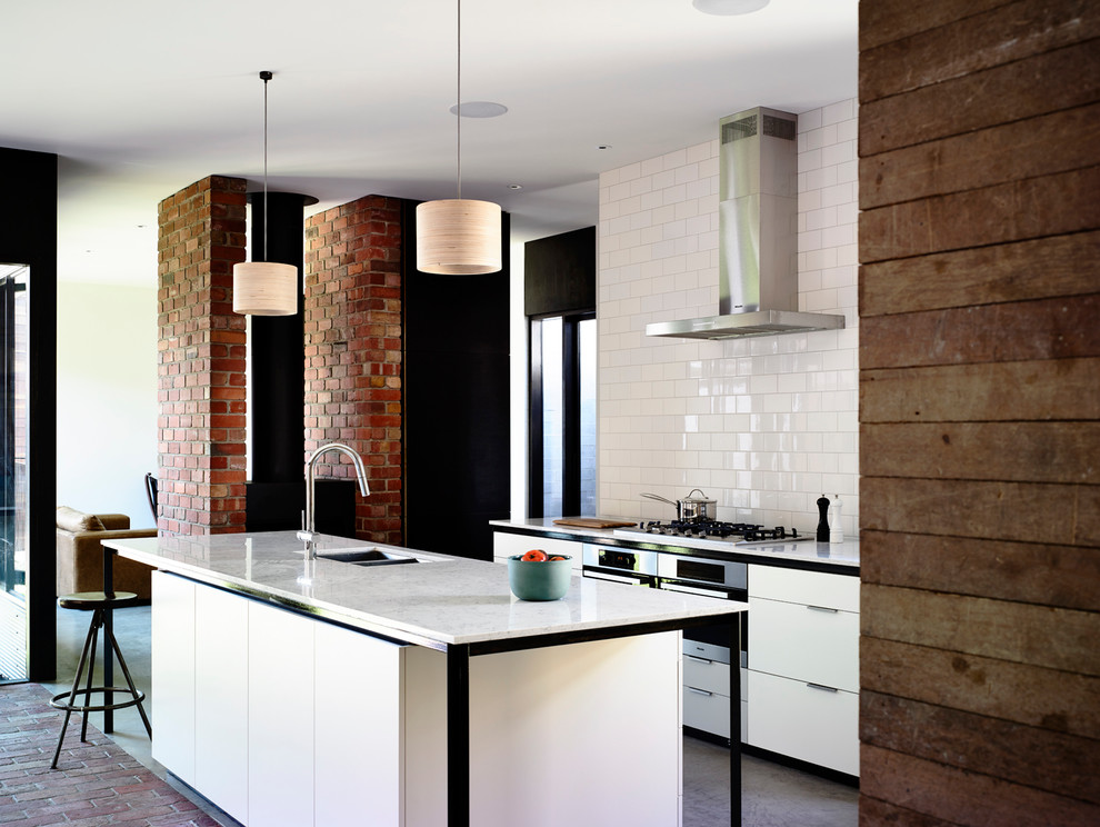 Photo of a mid-sized contemporary galley eat-in kitchen in Melbourne with concrete floors, with island, an undermount sink, flat-panel cabinets, white cabinets, quartz benchtops, white splashback, subway tile splashback and stainless steel appliances.