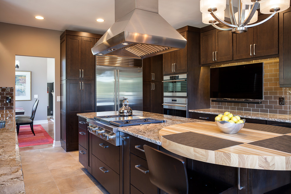 Expansive arts and crafts u-shaped open plan kitchen in Denver with an undermount sink, shaker cabinets, dark wood cabinets, granite benchtops, brown splashback, glass tile splashback, stainless steel appliances, ceramic floors and with island.