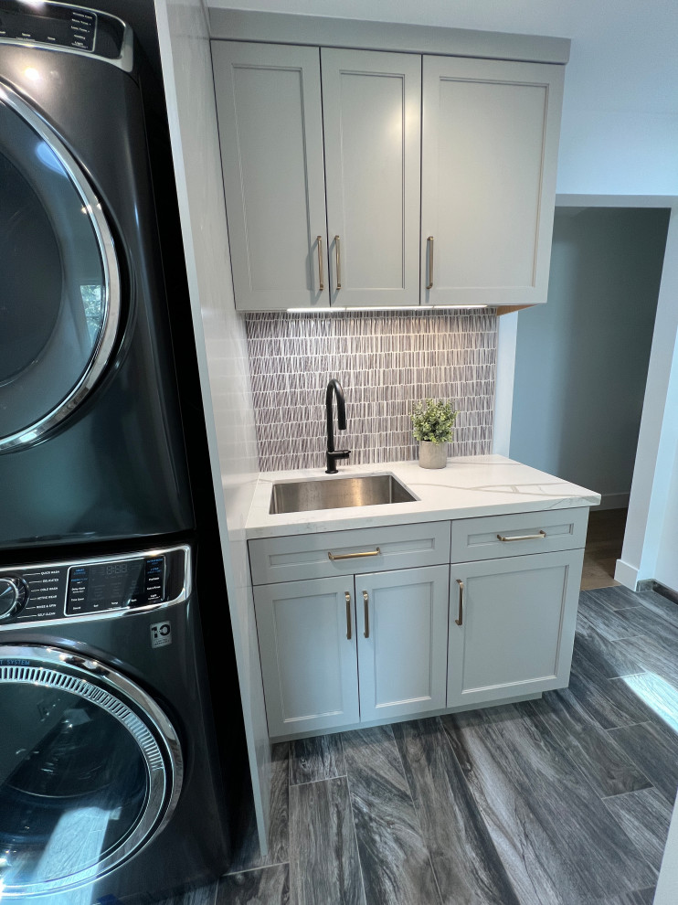 Small contemporary single-wall utility room in San Francisco with a submerged sink, shaker cabinets, grey cabinets, engineered stone countertops, multi-coloured splashback, porcelain splashback, white walls, porcelain flooring, a stacked washer and dryer, grey floors and white worktops.