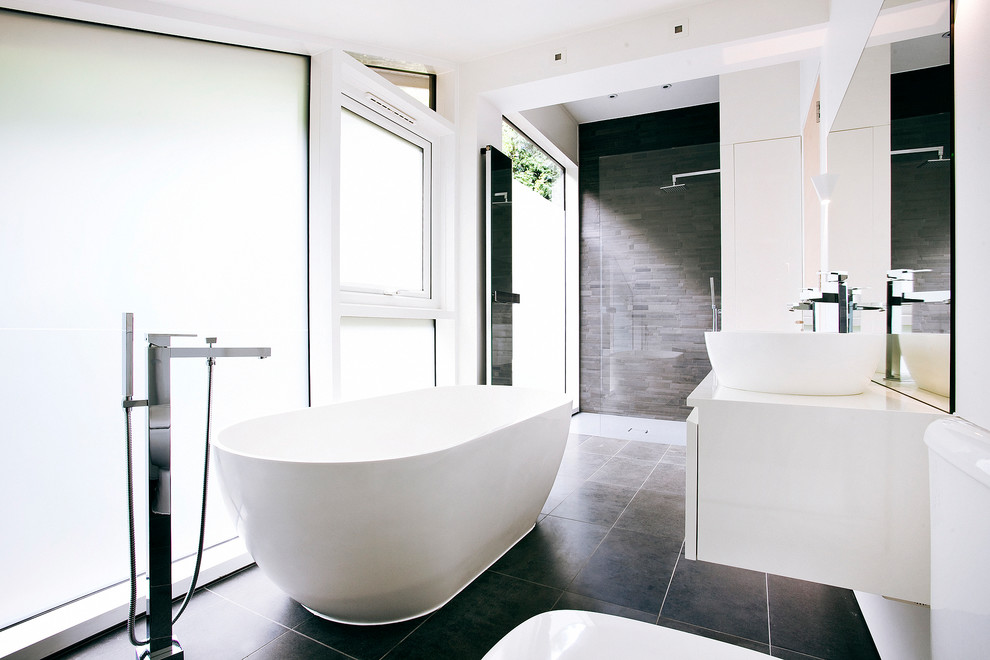 Mid-sized modern master bathroom in Surrey with flat-panel cabinets, white cabinets, a freestanding tub, white walls, a vessel sink, black floor, a curbless shower, black tile, stone tile and an open shower.