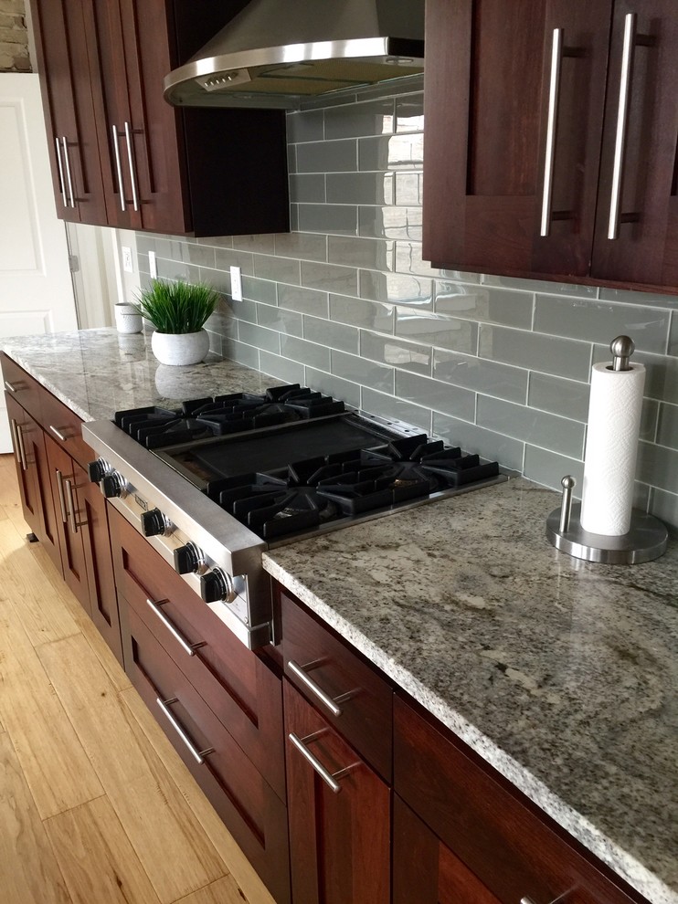 Kitchen - transitional light wood floor kitchen idea with shaker cabinets, dark wood cabinets, granite countertops, gray backsplash, glass tile backsplash and stainless steel appliances