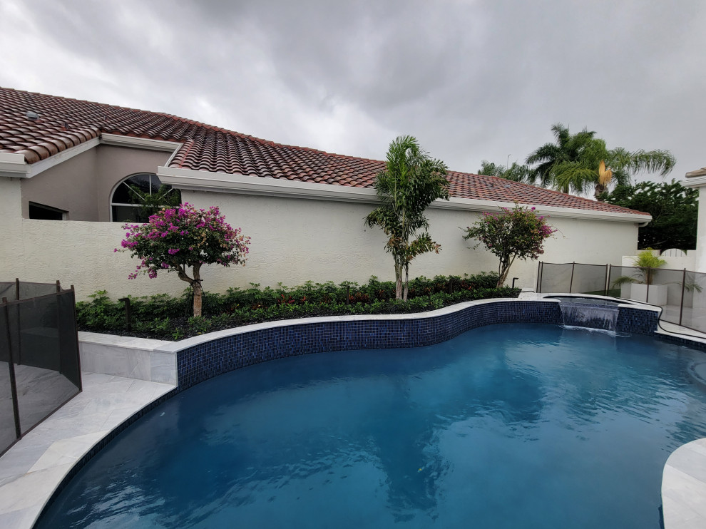 Medium sized modern courtyard kidney-shaped natural swimming pool in Miami with with pool landscaping and natural stone paving.