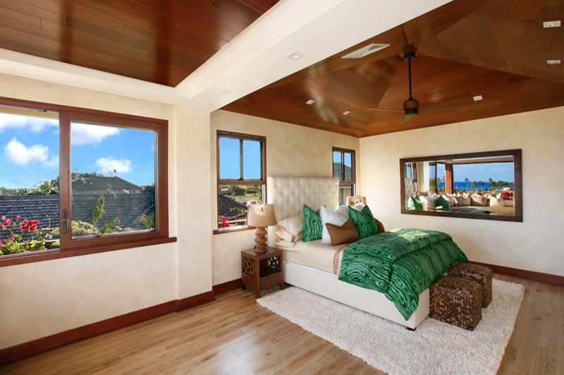 Expansive tropical master bedroom in Hawaii with beige walls and light hardwood floors.