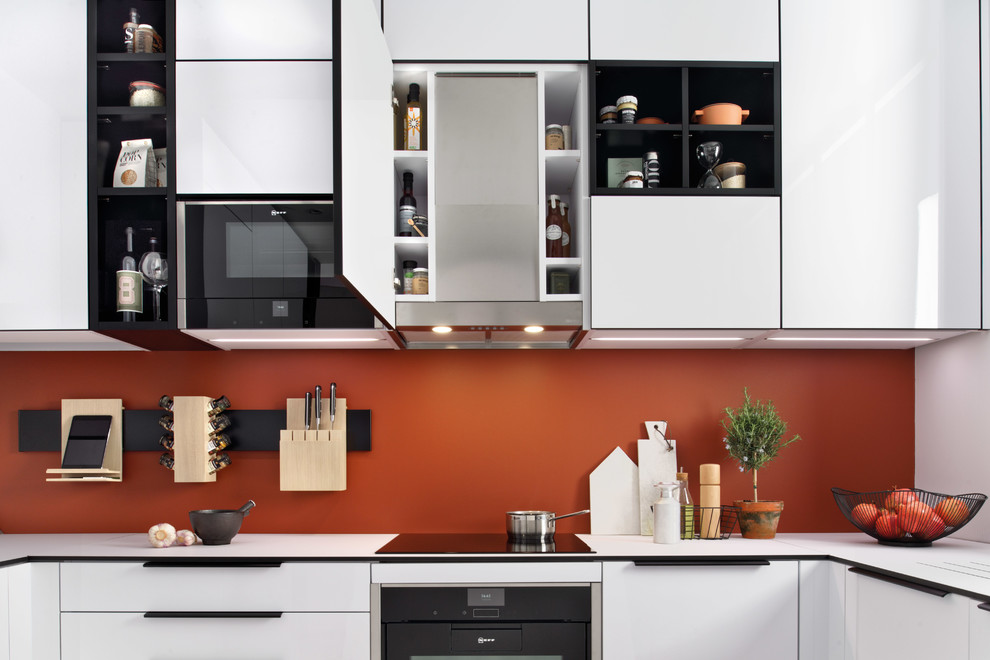 Photo of a small modern u-shaped eat-in kitchen in Surrey with a single-bowl sink, flat-panel cabinets, white cabinets, laminate benchtops, orange splashback, stainless steel appliances, terra-cotta floors, a peninsula, multi-coloured floor and white benchtop.