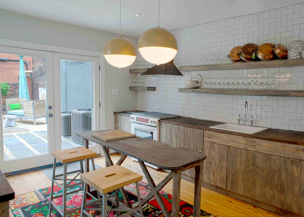 This is an example of a mid-sized eclectic separate kitchen in Philadelphia with a single-bowl sink, flat-panel cabinets, medium wood cabinets, wood benchtops, white splashback, subway tile splashback, white appliances, light hardwood floors and with island.