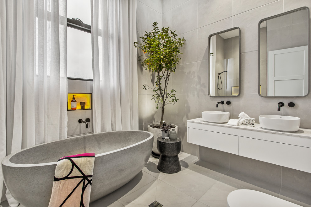 Contemporary bathroom in Melbourne with flat-panel cabinets, white cabinets, a freestanding tub, grey walls, a vessel sink, grey floor and white benchtops.