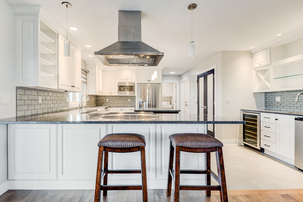 Design ideas for a mid-sized transitional u-shaped eat-in kitchen in Chicago with a farmhouse sink, raised-panel cabinets, white cabinets, quartzite benchtops, grey splashback, glass tile splashback, stainless steel appliances, ceramic floors, with island and beige floor.