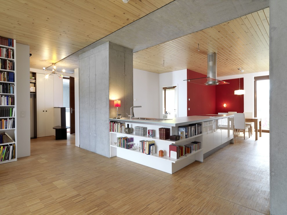 Large contemporary l-shaped open plan kitchen in Berlin with a drop-in sink, flat-panel cabinets, white cabinets, concrete benchtops, medium hardwood floors and a peninsula.