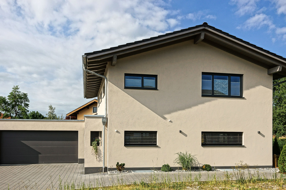 Photo of a mid-sized contemporary two-storey stucco beige house exterior in Other with a gable roof and a tile roof.