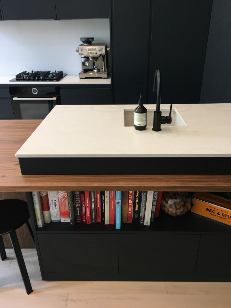 Photo of a small contemporary galley open plan kitchen in London with flat-panel cabinets, black cabinets, quartzite benchtops, white splashback, with island and white benchtop.