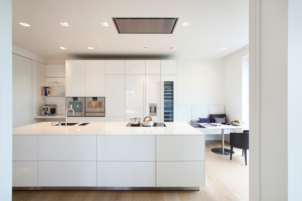 Photo of a large contemporary open plan kitchen in Cologne with a drop-in sink, flat-panel cabinets, white cabinets, panelled appliances, medium hardwood floors, with island and white splashback.
