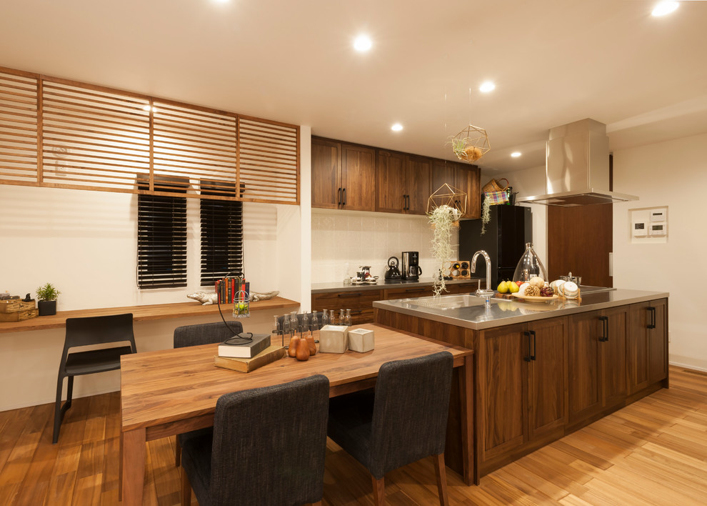 Inspiration for an asian galley open plan kitchen in Other with an integrated sink, shaker cabinets, dark wood cabinets, stainless steel benchtops, white splashback, black appliances, light hardwood floors, with island and beige floor.