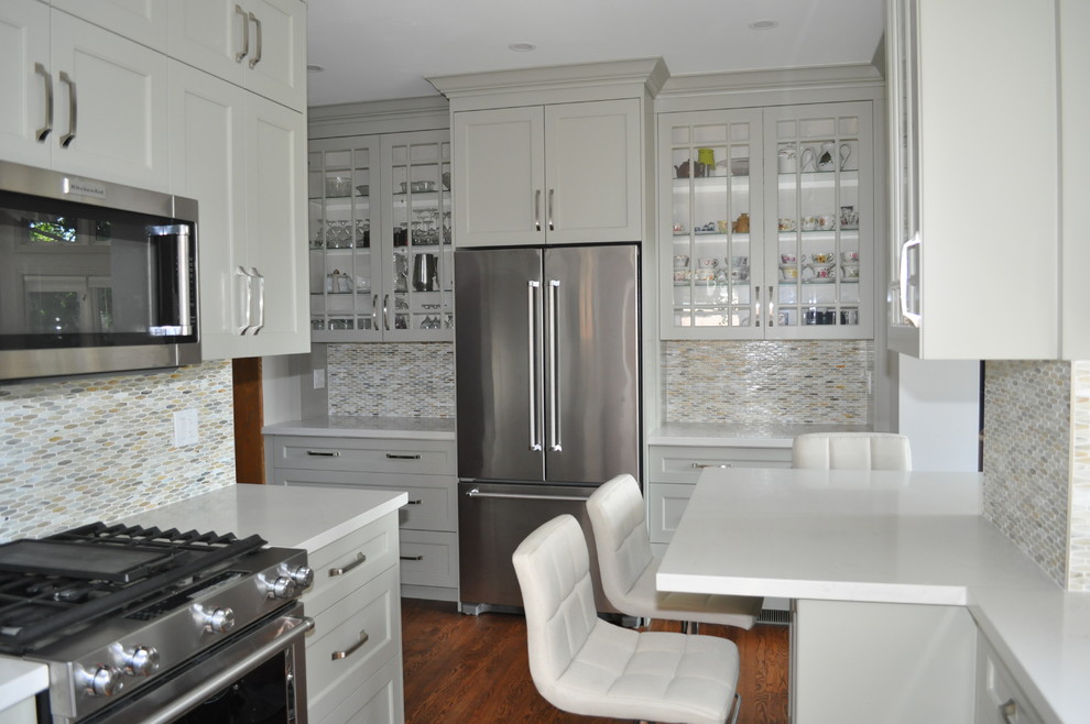 Example of a mid-sized transitional galley medium tone wood floor and brown floor eat-in kitchen design in Toronto with an undermount sink, shaker cabinets, green cabinets, quartz countertops, green backsplash, mosaic tile backsplash, stainless steel appliances and a peninsula