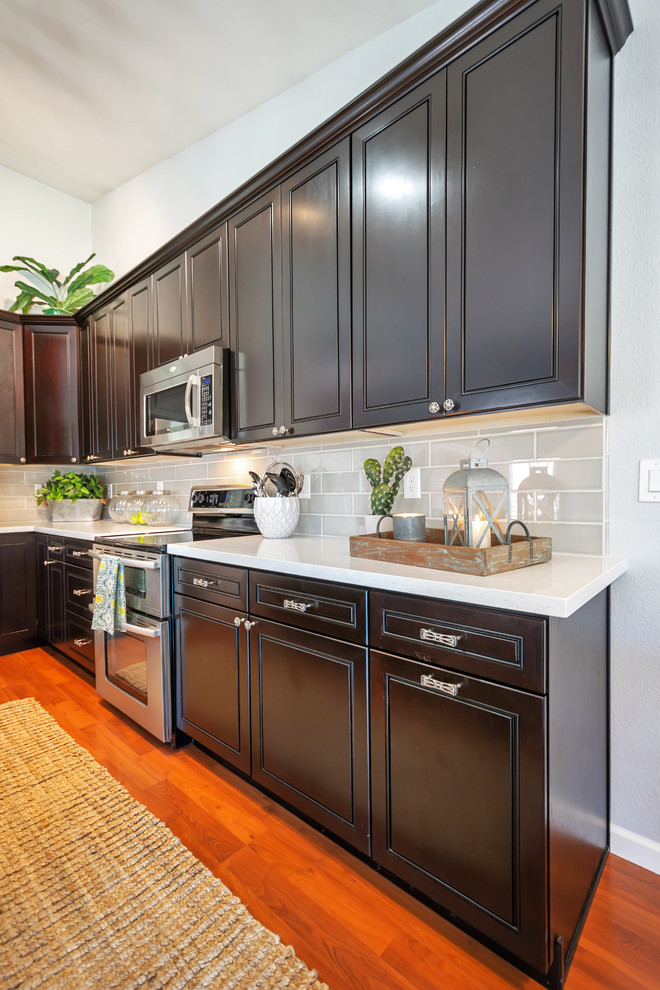 Inspiration for a mid-sized transitional l-shaped eat-in kitchen remodel in Phoenix with an undermount sink, raised-panel cabinets, black cabinets, quartz countertops, gray backsplash, porcelain backsplash, stainless steel appliances, an island and white countertops