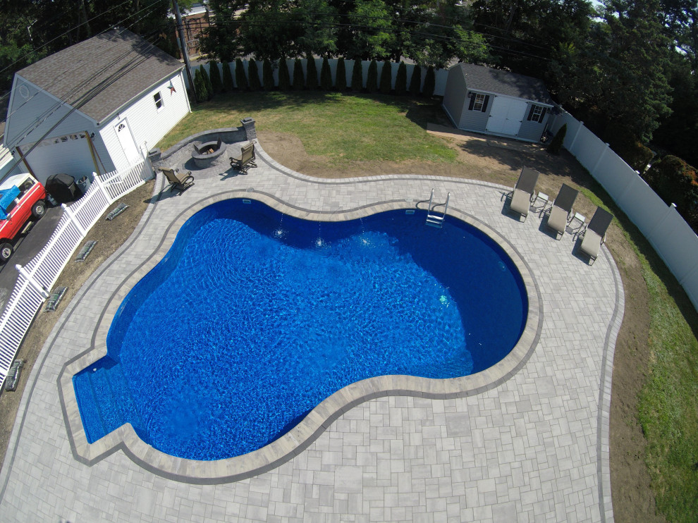 Photo of a large contemporary backyard custom-shaped natural pool in New York with concrete pavers.