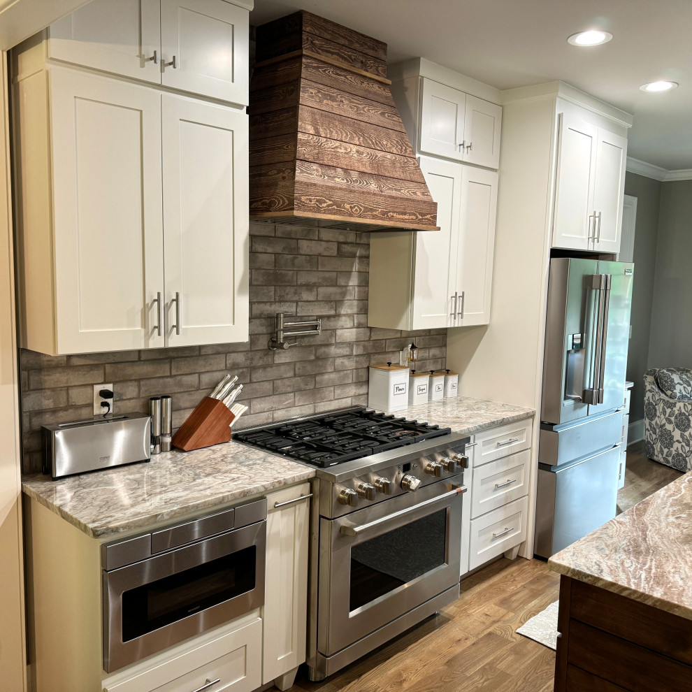 Example of a transitional galley medium tone wood floor and brown floor eat-in kitchen design in Atlanta with an undermount sink, shaker cabinets, white cabinets, granite countertops, gray backsplash, ceramic backsplash, stainless steel appliances, an island and multicolored countertops