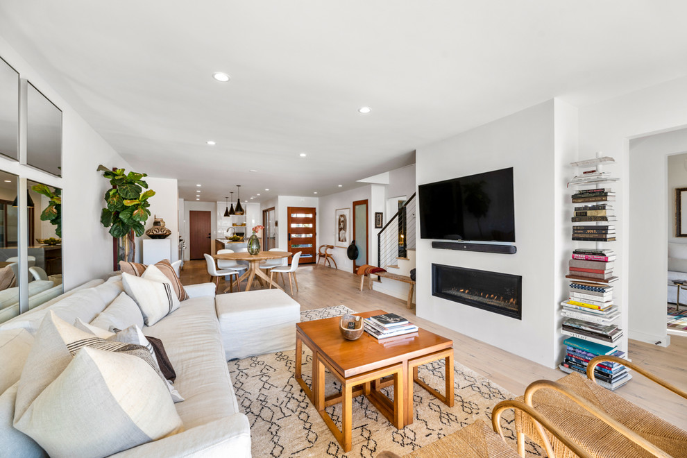 Large contemporary open concept living room in Los Angeles with white walls, light hardwood floors, a ribbon fireplace, a wall-mounted tv and beige floor.