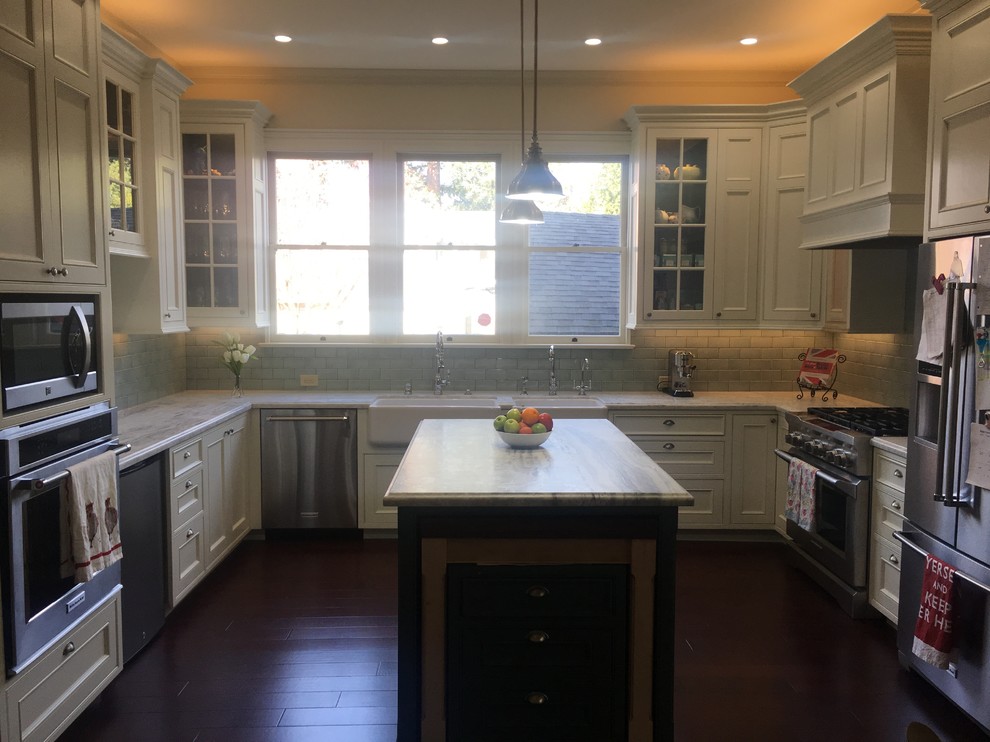 This is an example of a large traditional u-shaped eat-in kitchen in Other with a farmhouse sink, recessed-panel cabinets, beige cabinets, quartzite benchtops, green splashback, subway tile splashback, stainless steel appliances, dark hardwood floors, with island, multi-coloured floor and multi-coloured benchtop.