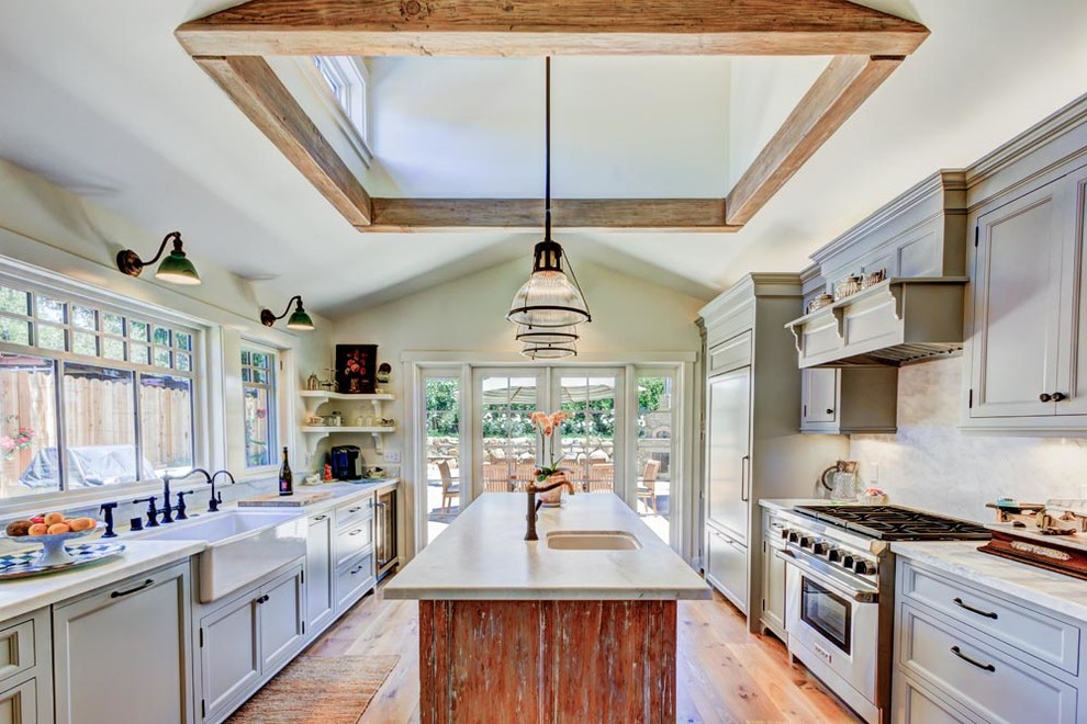 Design ideas for a large beach style u-shaped eat-in kitchen in Santa Barbara with a farmhouse sink, recessed-panel cabinets, beige cabinets, stainless steel appliances, light hardwood floors, with island, marble benchtops and stone slab splashback.