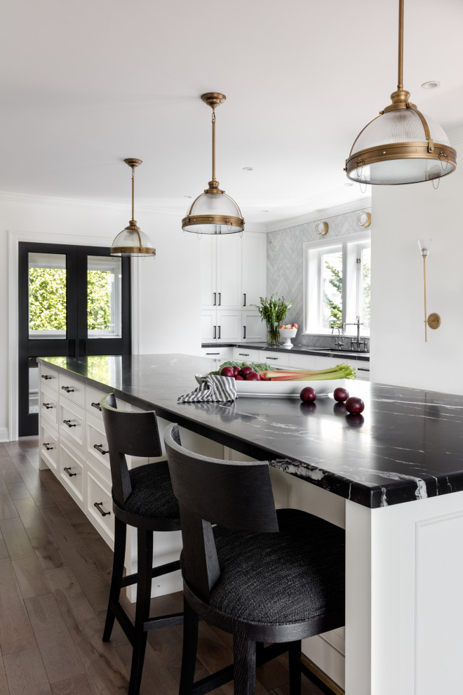 This is an example of a large traditional enclosed kitchen in Seattle with a submerged sink, beaded cabinets, white cabinets, marble worktops, grey splashback, marble splashback, black appliances, medium hardwood flooring, an island, brown floors and black worktops.