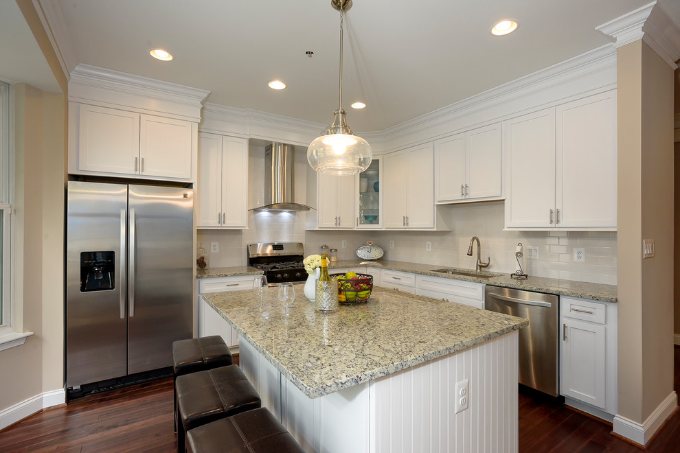 Mid-sized transitional l-shaped eat-in kitchen in Baltimore with an undermount sink, shaker cabinets, white cabinets, granite benchtops, beige splashback, ceramic splashback, stainless steel appliances, dark hardwood floors, with island and red floor.