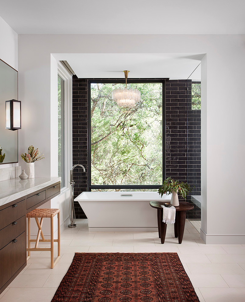 Inspiration for a contemporary bathroom in Austin with flat-panel cabinets, dark wood cabinets, a freestanding tub, black tile, subway tile, white walls, beige floor and white benchtops.